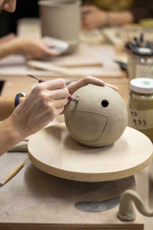 Mani di una ragazza mentre incide una sfera in argilla durante il workshop di ceramica in gres a Milano in Lombardia