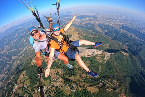 Due ragazzi sorvolano in parapendio biposto le montagne bergamasche in Lombardia sullo sfondo si intravede la Pianura Padana